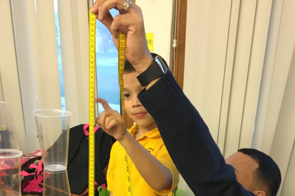 A teacher helps a young boy measure the height of a stack of cups