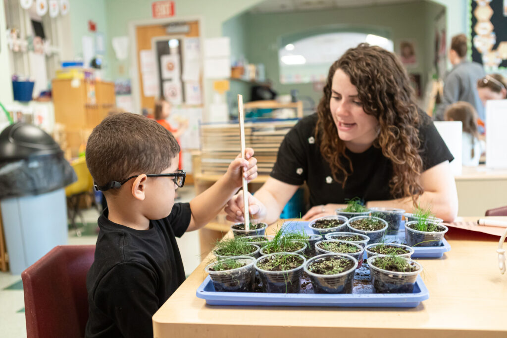 A teacher helps a boy measure plant growth in a classroom.