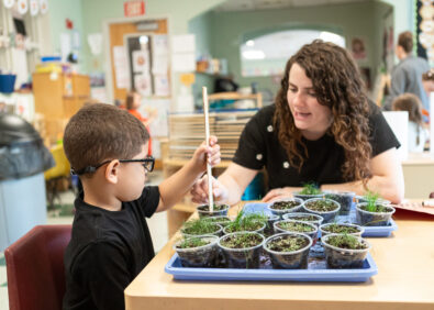 A teacher helps a boy measure plant growth in a classroom.