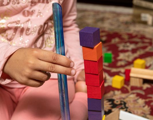 A child measuring a stack of colorful cubes with a rules