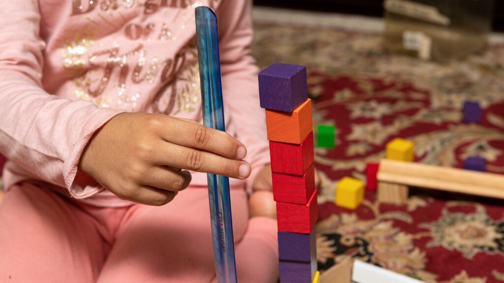 A child measuring a stack of colorful cubes with a rules